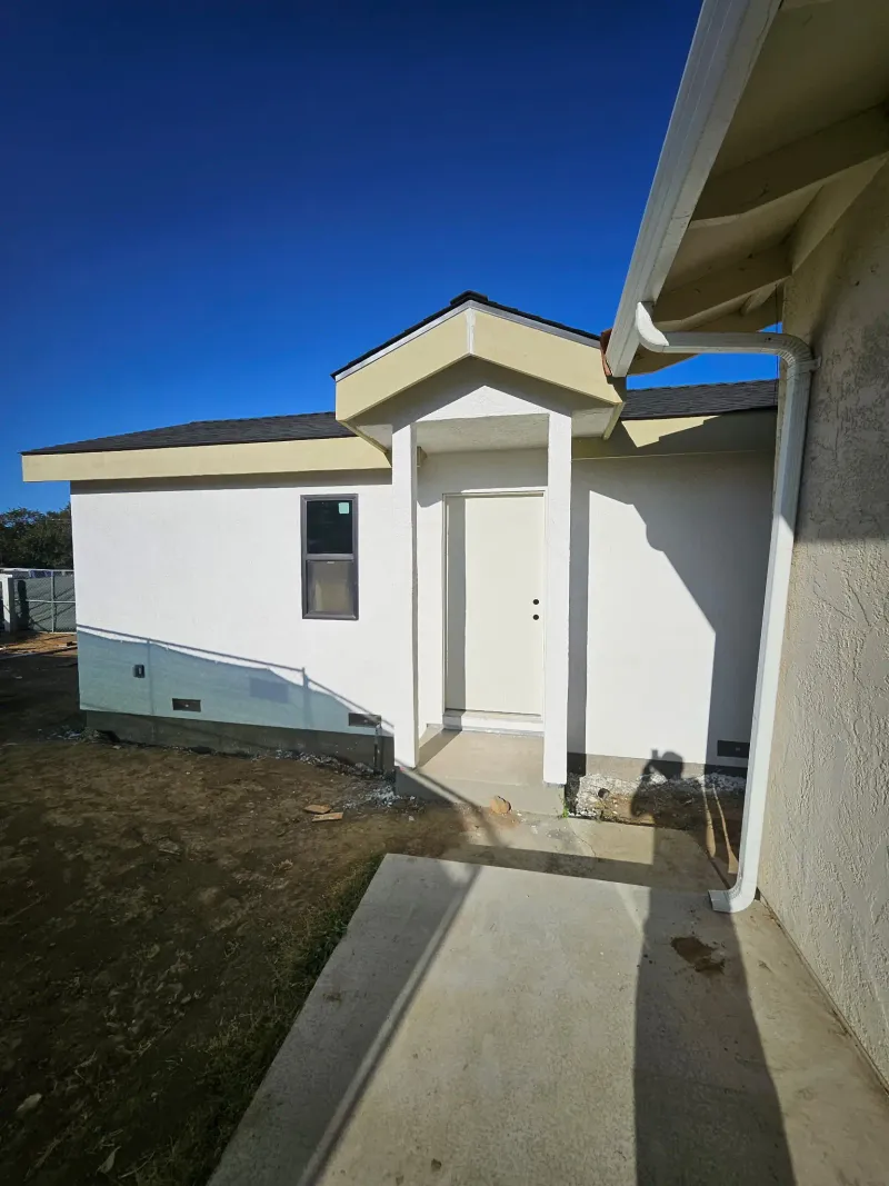 Finished white stucco ADU with a covered front entry and black window frames