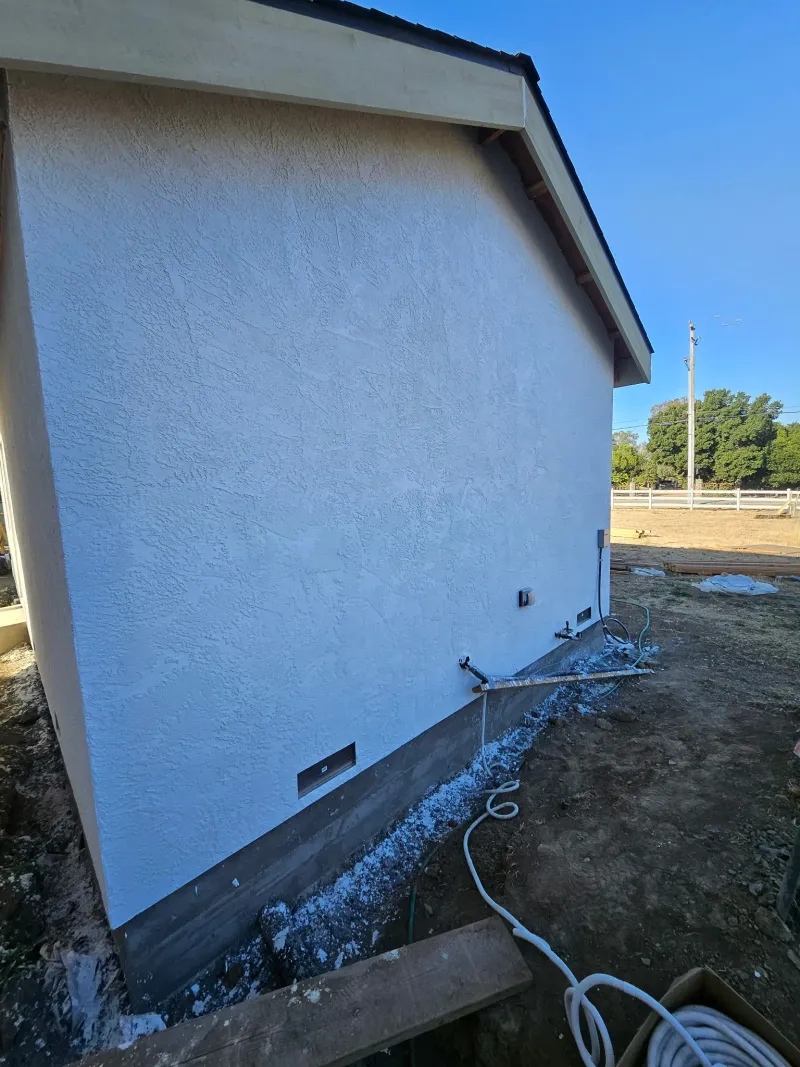 Rear gable of the stucco ADU with utility stubs at the base